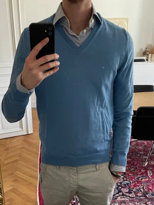 Burberry tröja - Ljusblå v-ringad tröja från burberry med lappar på armbågarna. Haft den ett tag, därav rätt så använd. Dock inga skador. 