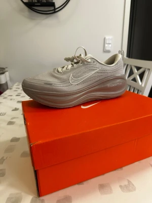 Nike Vomero Plus grå löparskor 44,5 Eu - Nike ZoomX sneakers i ljusgrått med vit swoosh och tjock, vågig sula för extra komfort. Ovandelen är i meshmaterial som andas och skon har klassisk snörning. Snygg och futuristisk design som sticker ut.       OBS SKORNA LIGGER UTE PÅ FLERA FÖRSÄLJNINGSSIDOR!