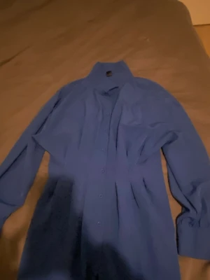 Blå klassisk skjorta med knappar - En stilren blå skjorta med lång ärm och knäppning framtill. Skjortan har klassisk krage och är perfekt för en clean och enkel look. Passar till många olika outfits och är ett måste i garderoben.