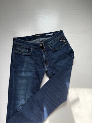 Mörkblå jeans från Replay - Snygga mörkblå jeans från Replay med klassisk femficksdesign och raka ben. Jeansen har detaljerade sömmar, dragkedjegylf och Replay-logga på bakfickan samt en patch i läderimitation bak. Tillverkade i slitstarkt denimtyg. W31 L32