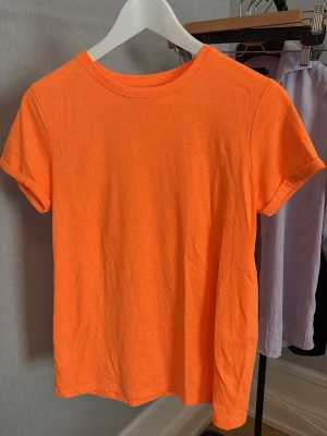 Orange basic t-shirt i bomull - En enkel och fräsch orange t-shirt med rund hals och korta ärmar. Perfekt för en avslappnad stil och lätt att matcha med jeans eller shorts. Tillverkad i mjuk bomull för skön komfort.