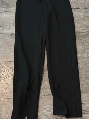 Svarta leggings med slits framtill - Snygga svarta leggings med trendiga slitsar framtill vid bensluten. De har en tight passform och är gjorda i ett stretchigt material som sitter bekvämt. Perfekta att matcha med sneakers eller boots för en modern vibe.