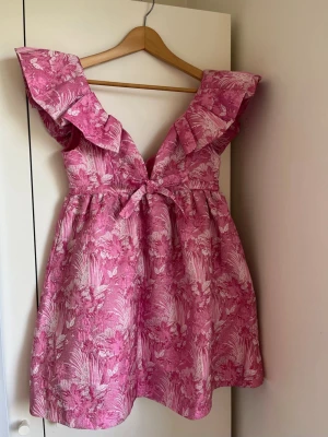 ROSA SOMMARKLÄNNING - Otroligt gullig v-ringad klänning som är perfekt till studentmottagningar, midsommar och varför inte alla andra festligheter i sommar! Rosa mönster med glitter och en rosett, dragkedja i ryggen. Denna klänning har aldrig blivit använd då den var för stor för mig så beställde den i en storlek mindre istället. 