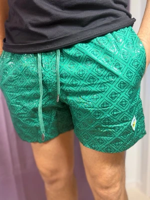 Gröna badbyxor med mönster - Snygga gröna badbyxor från Scotch & Soda med geometriskt mönster i svart och logopatch på benet. De har dragsko i midjan och sidofickor. Perfekta för strand eller pool och tillverkade i snabbtorkande material.