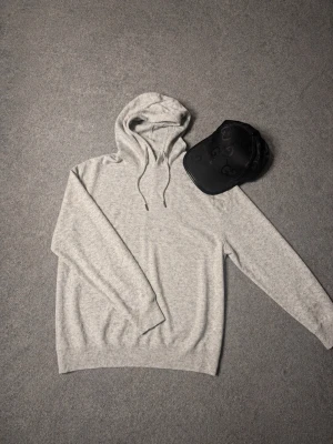Ljusgrå merinohoddie med huva - En stilren ljusgrå merinohoodie med huva och dragsnören. Tillverkad i mjukt och bekvämt material, perfekt för en avslappnad look. Hoodien har långa ärmar och ribbade muddar vid ärmslut och nederkant. Passar perfekt till jeans eller sweatpants. Pris diskuteras 🫡
