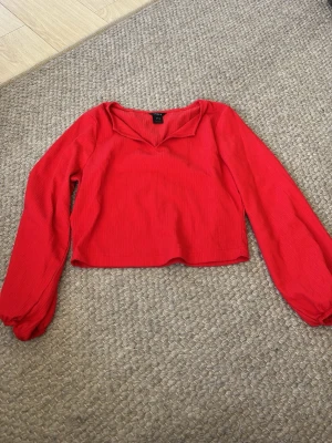 Röd croppad topp med v-ringning - Säljer en röd croppad topp från Lindex med v-ringning och långa ärmar. Toppen är ribbad och har en snygg, enkel design som passar perfekt till jeans eller kjol. Materialet är mjukt och stretchigt, vilket gör den bekväm att bära.