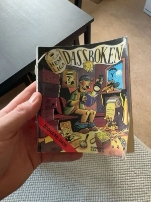 Hemliga Dassboken - Rolig och färgglad bok med titeln 'Hemliga Dassboken Kodnamn: Dass' från Bonnier Carlsen. Omslaget har tecknade illustrationer och boken är försedd med ett snöre för upphängning. Perfekt för den som vill ha något att läsa på toaletten.