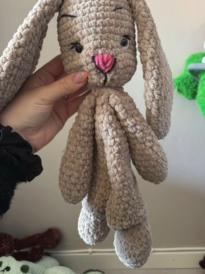 Beige virkad kaninmjukis - Supergullig beige kaninmjukis med långa öron och rosa nos. Den är virkad i ett mjukt, fluffigt garn och har safety ögon och detaljer. Perfekt som gosedjur eller snuttefilt. 