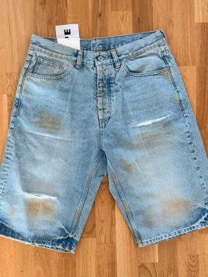 Ljusblå denimshorts från HOPE - Säljer ett par ljusblå denimshorts från HOPE med avslappnad passform och slitna detaljer framtill. Klassisk femficksmodell med knappgylf och bälteshällor. Perfekta för sommaren och ger en cool, vintagekänsla.