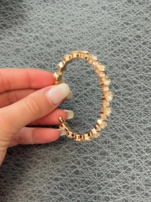 Guldigt armband med pärlor - Snyggt armband i guldfärgad metall med genomskinliga pärlor som ger en lyxig känsla. Armbandet har en elastisk design som gör det enkelt att ta på och av. Perfekt accessoar för att lyfta din outfit med lite extra bling.