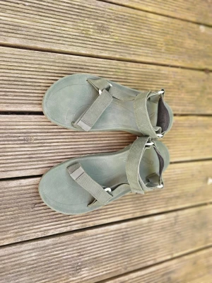 Gröna Teva sandaler med remmar - Snygga gröna sandaler från Teva med justerbara remmar i textil och bekväm sula i gummi. Perfekta för sommaren med sin sportiga och minimalistiska design. Kardborrestängning runt vristen och över foten för bra passform.