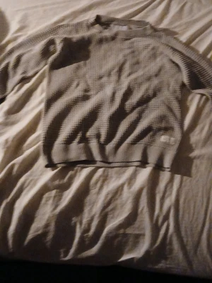 Grå ribbad tröja från Carhartt - Säljer en stilren grå tröja från Carhartt med ribbade muddar och diskret logga vid nederkanten. Tröjan har en klassisk rund hals och är tillverkad i ett mjukt, strukturerat material som ger en avslappnad look.