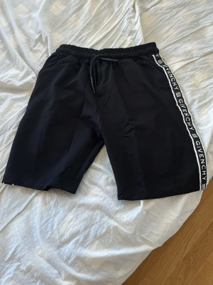 Svarta shorts från Givenchy sällsynt  - Svarta shorts från Givenchy med vit logotyptext längs sidorna och elastisk midja med snörning. Klassisk en sportig vibe, perfekta för sommaren. Slim-fit