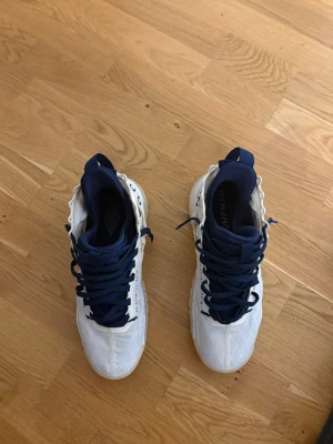 Vita och marinblå Jordan sneakers - Snygga sneakers från Jordan i vitt med marinblå detaljer och snörning. Skorna har högt skaft och tydlig Jumpman-logga på insidan. Ovandelen är i textil och syntet, vilket ger en sportig och modern look.