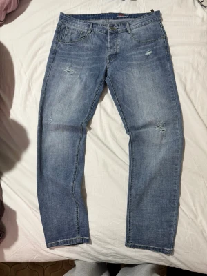 Ljusblå slitna jeans med raka ben - Snygga ljusblå jeans med raka ben och slitningar på låren och knäna. Klassisk femficksmodell med normal midja och dragkedjegylf. Perfekta för en avslappnad och trendig look.