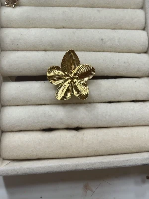 Justerbar Guld blom ring - Snygg ring i guldfärgad metall med en stor blomformad design. Blomman har fem blad med detaljerade räfflor som ger en cool och unik look. Perfekt accessoar för att lyfta din outfit med en touch av blommig stil. Säljer för 50-100kr