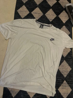 Vit Nike Dri-Fit t-shirt 3XL - Säljer en vit Nike Dri-Fit t-shirt i storlek 3XL. T-shirten har korta ärmar, rund halsringning och är tillverkad i ett lätt och ventilerande material med små hål för extra andningsförmåga. Nike-logga på bröstet för en sportig look.