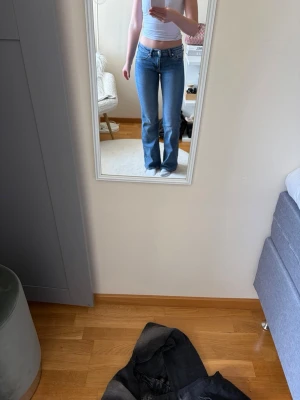 Blå bootcut jeans med låg midja - Säljer ett par klassiska blå bootcut jeans med låg midja och fem fickor. Jeansen har en snygg tvätt och sitter tajt över låren men är utsvängda nedtill. Perfekta till crop tops eller hoodies för en chill look.