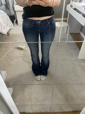 Mörkblå bootcut jeans med låg midja - Säljer ett par mörkblå bootcut jeans med låg midja och klassisk femficksdesign. Jeansen har en lätt tvättad look och sitter tajt över låren med utsvängda ben. Perfekta för en avslappnad och trendig stil.