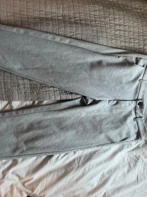 Gråa kostymbyxor från Lindbergh - Snygga gråa kostymbyxor från Lindbergh i slim fit-modell. Byxorna har klassisk design med bälteshällor, knapp och dragkedja framtill. Perfekta för en stilren look och passar till skjorta eller t-shirt.