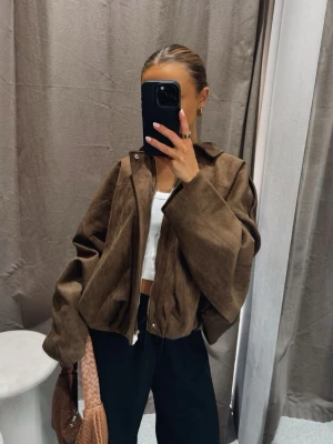 Brun mockajacka med dragkedja - Snygg brun mockajacka med dragkedja framtill och oversized passform. Jackan har långa ärmar och en klassisk krage, perfekt för att lyfta din outfit med en trendig touch.