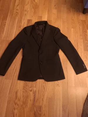 Svart kostym med kavaj och byxor - Stilren svart kostym med klassisk kavaj och matchande byxor. Kavajen har två knappar och fickor framtill, perfekt för en dressad look. Byxorna är raka och enkla att matcha. Passar dig som vill ha en tidlös och snygg outfit. Kan gå ner i pris om varan köps innan 16 maj
