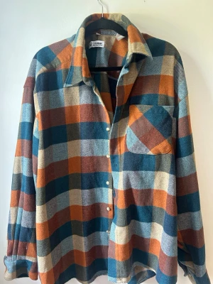 Vintage flanellskjorta  - Skjortan har ett karaktäristiskt blockmönster och är tillverkad i ett strukturerat material. Den har en klassisk krage, knäppning framtill och en bröstficka på vänster sida. Vintage flanellskjorta från L’Homme Morderne