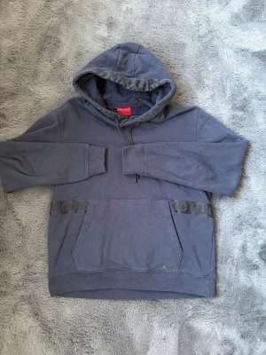 Blå hoodie från HUGO - Snygg blå hoodie från HUGO med diskret logga framtill och klassisk känguruficka. Hoodien har huva med dragsko och ribbade muddar. Perfekt för en avslappnad och trendig stil. Otroligt fin och använd max 5 gånger, skriv vid frågor eller funderingar.