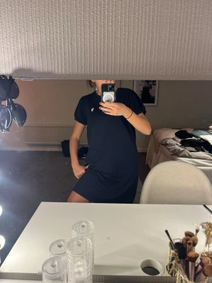 Mörkblå t-shirtklänning från Ralph Lauren - Mörkblå t-shirtklänning från Ralph Lauren med korta ärmar och klassisk passform. Klänningen har en liten vit broderad logga på bröstet och är gjord i mjukt bomullsmaterial. Perfekt för en avslappnad och stilren look.