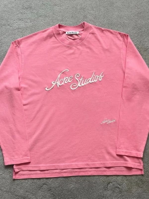 Rosa långärmad tröja Acne Studios - Säljer en rosa långärmad tröja från Acne Studios med stor vit broderad logga på bröstet och mindre logga nedtill. Tröjan har rund halsringning och är gjord i mjuk bomull. Perfekt för dig som gillar streetwear och vill sticka ut.