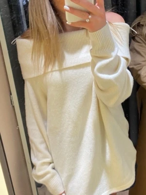 Off shoulder vit stickad tröja - Trendig off shoulder stickad tröja i mjuk vit färg. Oversized passform med bred krage som vilar över axlarna och långa ärmar. Perfekt för en avslappnad och stilren look.