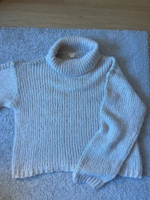 Beige stickad polotröja - Mysig beige stickad polotröja med grovstickad struktur och bred polokrage. Tröjan har långa ärmar och ribbade muddar vid ärmslut och nederkant. Perfekt för kalla dagar och enkel att styla med jeans eller kjol.