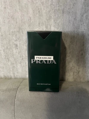 Prada Paradigme Eau de Parfum - Prada Paradigme Eau de Parfum i en elegant mörkgrön rektangulär förpackning med silverfärgade detaljer. Lyxig och stilren design som verkligen sticker ut på parfymhyllan. Perfekt för dig som gillar exklusiva dofter och snygga flaskor.