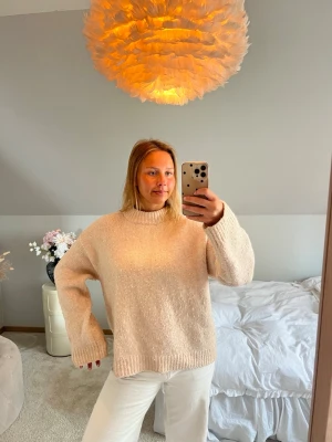 Beige oversized stickad tröja - Mysig beige stickad tröja med avslappnad passform och ribbade muddar vid ärmslut och nederkant. Tröjan har en högre rund halsringning och är perfekt för lager-på-lager-stil. Materialet känns mjukt och skönt mot huden.