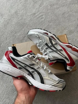 ASICS Gel Kayano 14 White/Classic Red - Snygga ASICS sneakers i vitt med svarta och röda detaljer. Ovandelen är i mesh och syntet för bra andningsförmåga och komfort. Klassisk sportig design med ASICS logga på sidorna och robust sula för extra stöd.
