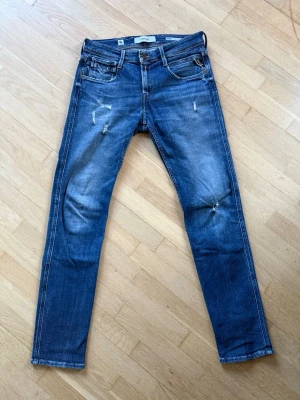 Replay Anbass Jeans  - Blåa slim fit jeans i modellen Anbass från märket Replay. Snygga slitningar på lår och knäet, tyvärr har de blivit hål vid knäet och därav priset annars är jeansen i bra skick. Skick: 7/10, Storlek: 30/32 