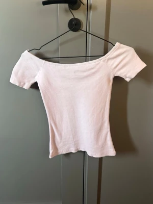 Ljusrosa offshoulder ribbad topp - Söt ljusrosa topp med offshoulder-design och korta ärmar. Toppen är ribbad och har en tight passform som framhäver figuren. Perfekt att styla med jeans eller kjol för en trendig look.