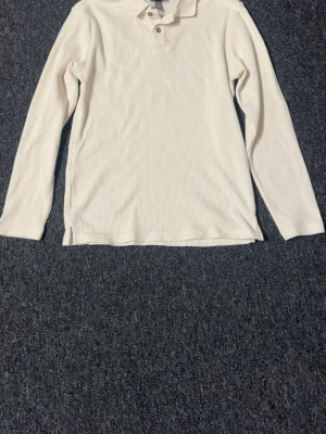 Vit långärmad piké från H&M - Vit långärmad pikétröja från H&M i slim fit-modell. Tröjan har klassisk krage, knappar vid halsen och är tillverkad i ett ribbat, mjukt material som känns skönt mot huden. Perfekt för en clean och stilren look.