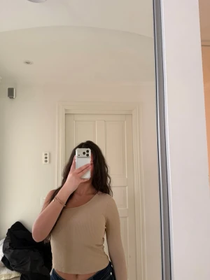 Beige ribbad oneshoulder topp - Trendig beige ribbad topp med oneshoulder-design och lång ärm. Croppad modell som sitter snyggt och framhäver figuren. Perfekt att styla med jeans eller kjol för en cool look.