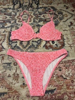 Rosa bikini med smockade detaljer - Superfin oanvänd rosa bikini med smockade detaljer och vadderad bygel-bh. Bikinin har justerbara axelband och hög midja på underdelen. Överdel i strl M & underdel i L! 👙⛅️