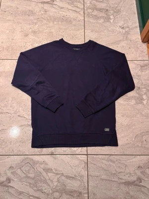 Mörkblå sweatshirt från blend  - En stilren mörkblå sweatshirt från blend med rund halsringning och ribbade muddar vid ärmslut och nederkant. Tröjan har en diskret blend-logga nertill. Perfekt för en avslappnad och cool look.