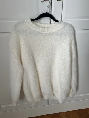 Vit fluffig stickad tröja från Nitted - Supermjuk och fluffig vit stickad tröja med rund halsringning och långa ärmar. Oversized passform som ger en avslappnad look. Perfekt för kalla dagar när du vill vara både varm och snygg. Tror att det är storlek S.