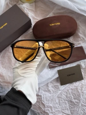 Tom Ford solglasögon med gula glas - Snygga solglasögon från Tom Ford med svart båge och gula glas. Klassisk aviatorform som ger en cool vibe. Kommer med originalfodral och putsduk. Perfekta för dig som vill sticka ut med stilrena accessoarer.