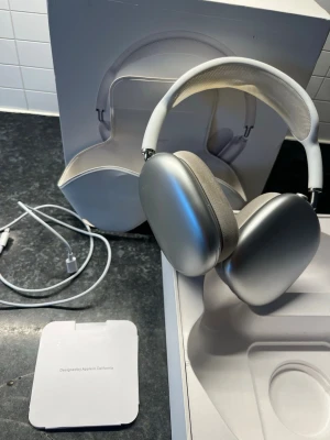 Apple AirPods Max silver hörlurar - Snygga och moderna Apple AirPods Max i silver med en stilren design. Hörlurarna har stora öronkåpor i aluminium, mjuka mesh-kuddar och ett justerbart huvudband i vitt tyg. Levereras med originalförpackning, laddkabel och smart case.