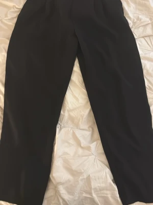 Svarta vida kostymbyxor - Stilrena svarta kostymbyxor med rak och vid passform. Byxorna har hög midja och klassisk design, perfekta för en dressad look. Materialet ser ut att vara ett mjukt tyg med lätt fall.