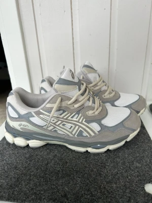 Asics gråvita sneakers mesh & mocka - Snygga sneakers från Asics i grått och vitt med beige detaljer. Ovandelen är i mesh och mocka för en sportig vibe och bra andningsförmåga. Klassisk Asics-logga på sidan och rejäl sula för skön komfort. Perfekta för dig som gillar stilrena och bekväma skor.