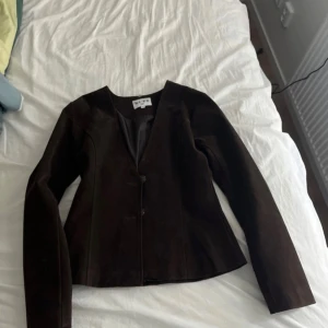 Brun mockajacka från NA-KD med fuskpäls - Säljer en brun mockajacka från Lovisa Worges kollektion med NA-KD.  Lång  ärm och snygg figursydd passform. Jackan har en avtagbar krage i brun fuskpäls och stängs med knappar framtill. Perfekt för dig som vill ha en trendig och unik jacka med coola detaljer. Slutsåld och aldrig använd .