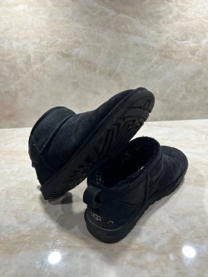 Svarta UGG S 41 - Svarta boots från UGG i mjuk mocka med låg skaft och värmande foder. Klassisk rund tå och grov sula för bra grepp. Perfekta för kalla dagar och enkel att dra på tack vare hällan bak. Skick 9/10
