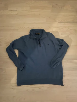 Blå halvzip-tröja från Polo Ralph Lauren - Snygg blå stickad tröja från Polo Ralph Lauren med halv dragkedja och broderad logga på bröstet. Tröjan har hög krage och långa ärmar, perfekt för lager-på-lager-stil. Klassisk och tidlös design som funkar året runt.