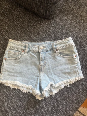 Ljusblå denimshorts med fransar - Snygga ljusblå denimshorts och råa fransade kanter. Klassisk femficksmodell med knapp och dragkedja framtill. Perfekta för varma dagar och enkel att matcha med allt. Storlek 34💞